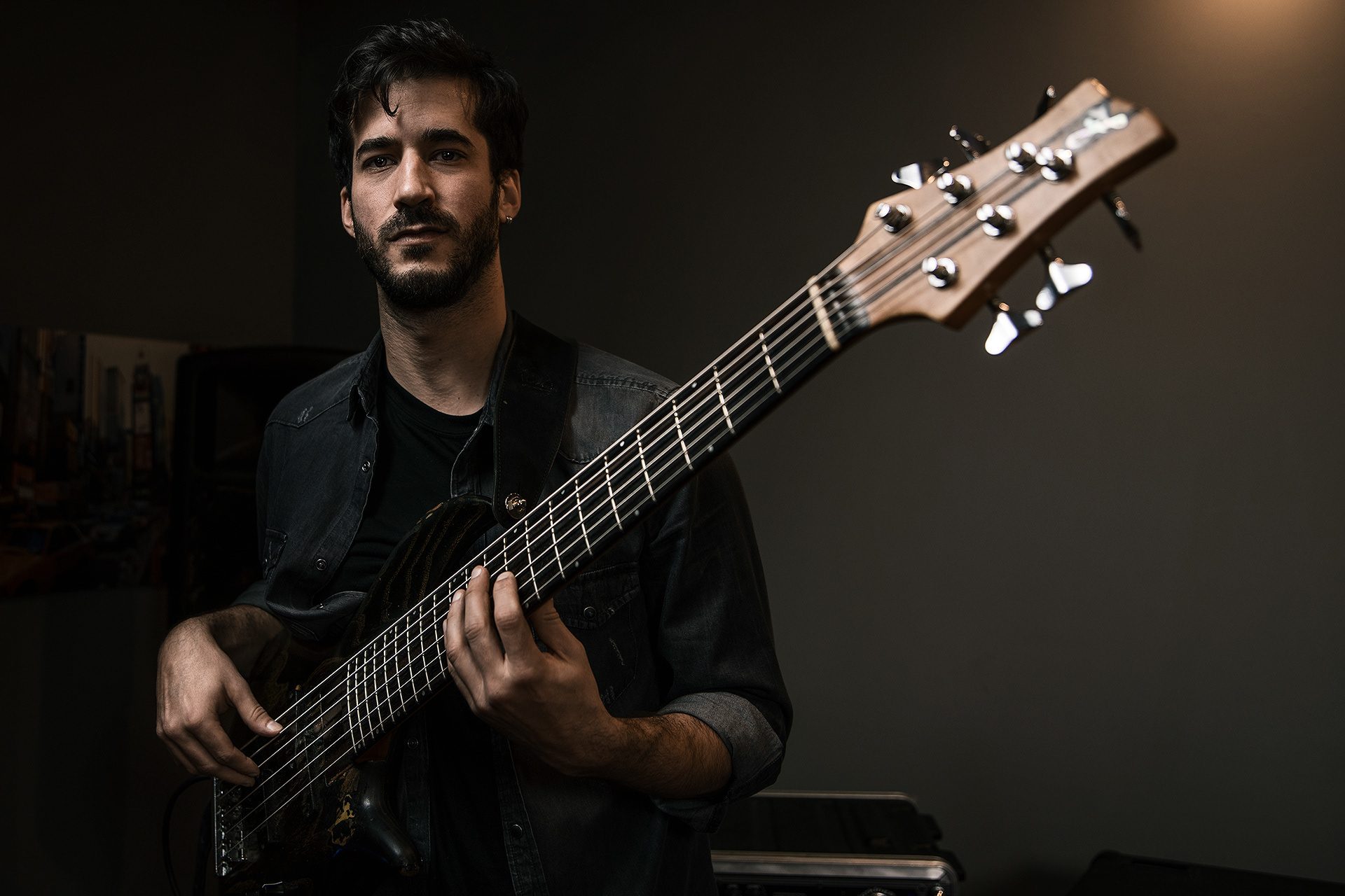 Un musicista che suona un basso a sei corde su fondo scuro