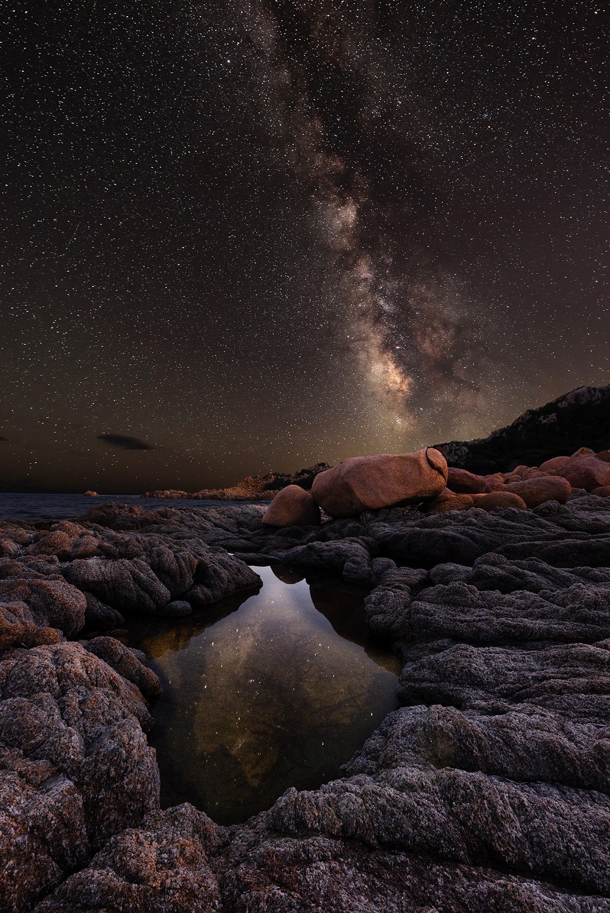 Una pozza d’acqua tra le rocce della costa che riflette la Via Lattea, Capo Comino, Sardegna