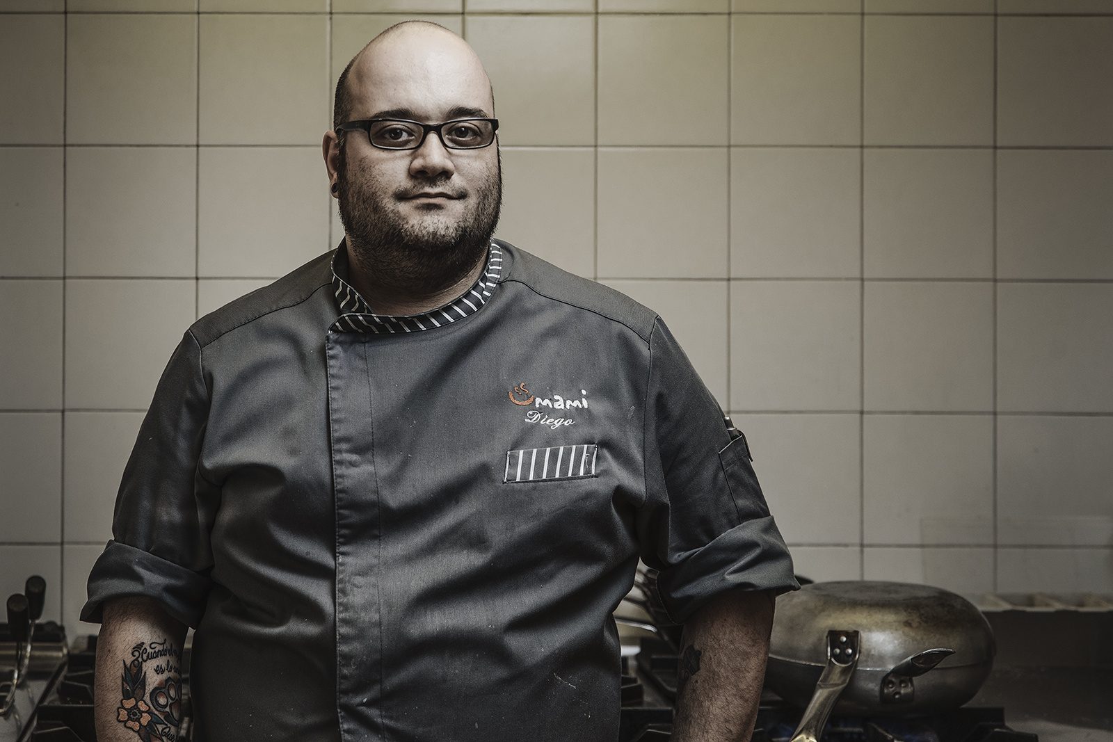 Lo chef in primo piano davanti alle piastrelle bianche della cucina