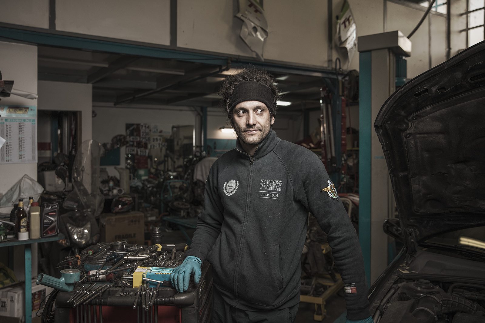 Un meccanico con i guanti accanto a un’auto con il cofano aperto, nella sua officina