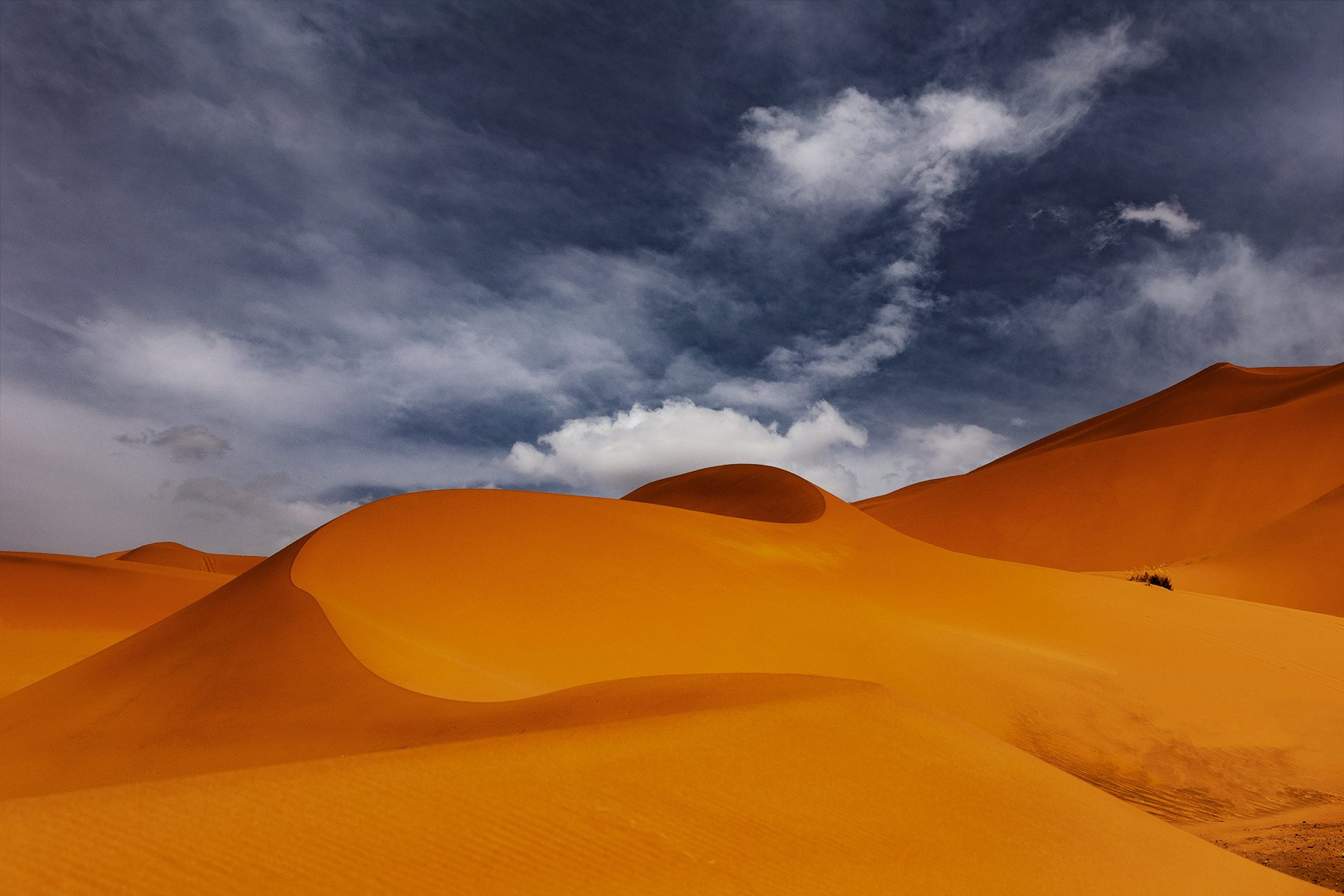Dune arancioni sotto un cielo scuro con nuvole bianche, Marocco