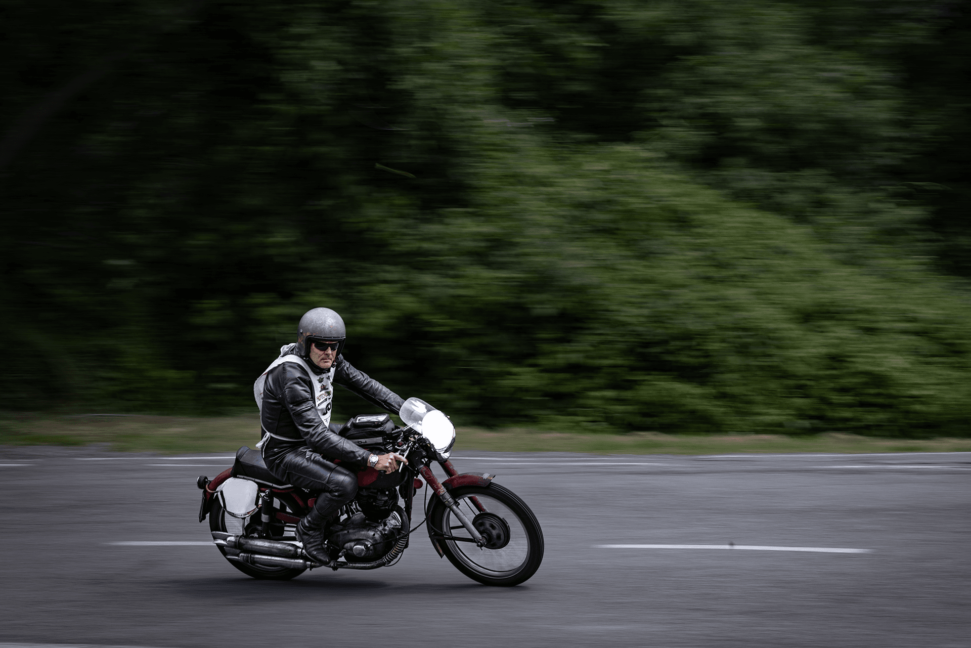 Motociclista su una moto d’epoca in strada, ripreso in movimento