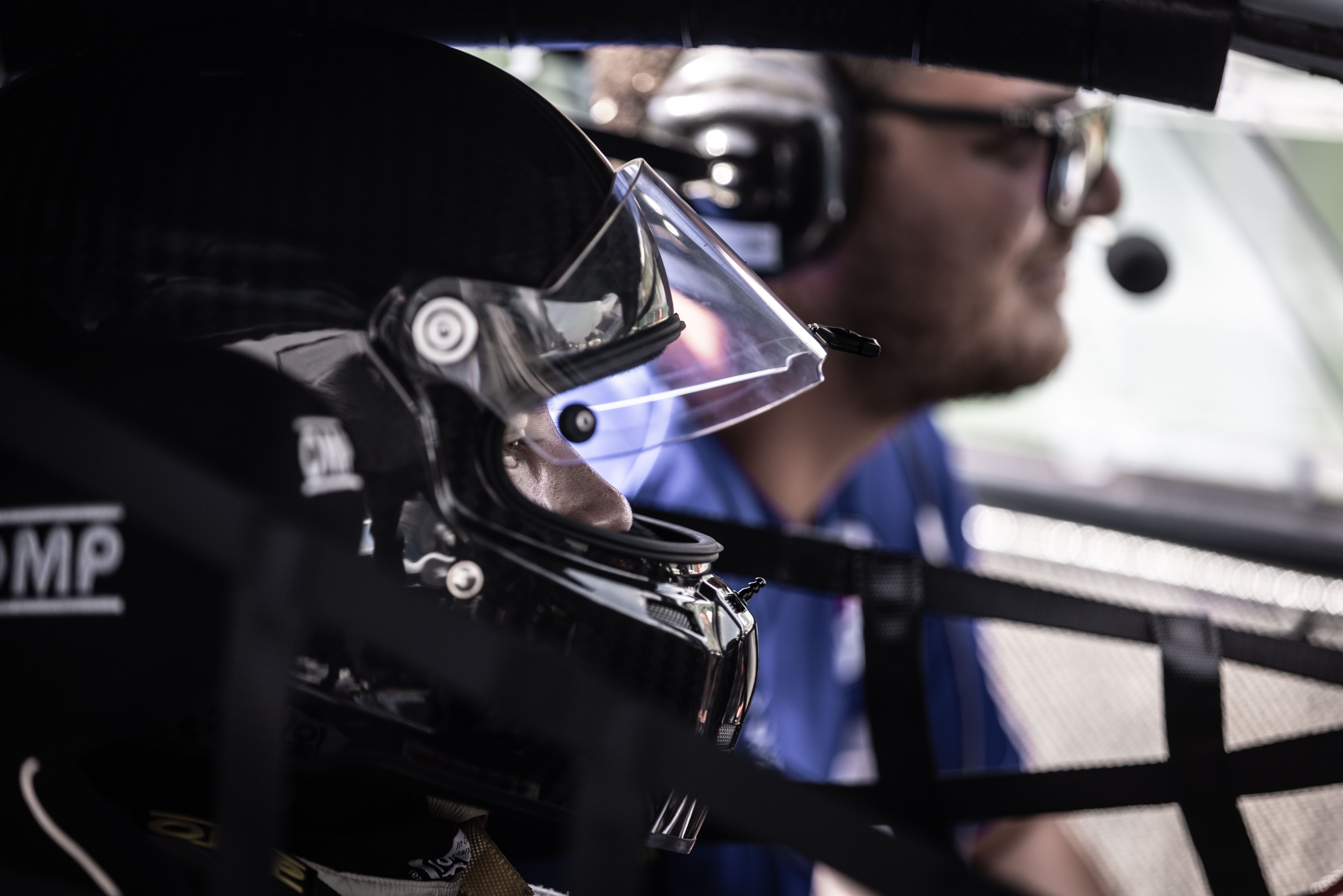 Pilota con il casco nell’abitacolo di un’auto da corsa, accanto a un tecnico con le cuffie