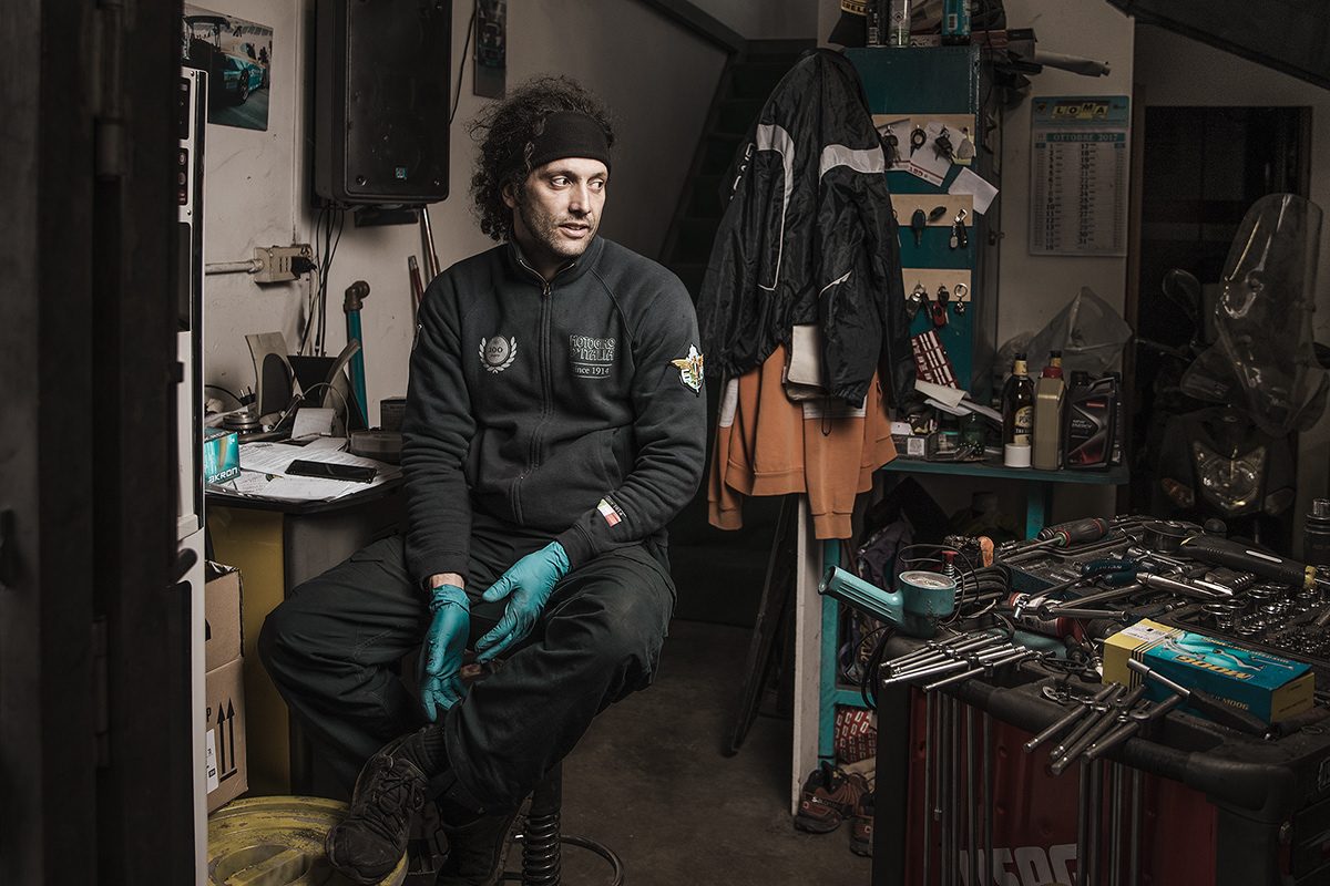 Meccanico con i guanti e la felpa del Motogiro d’Italia, seduto nella sua officina